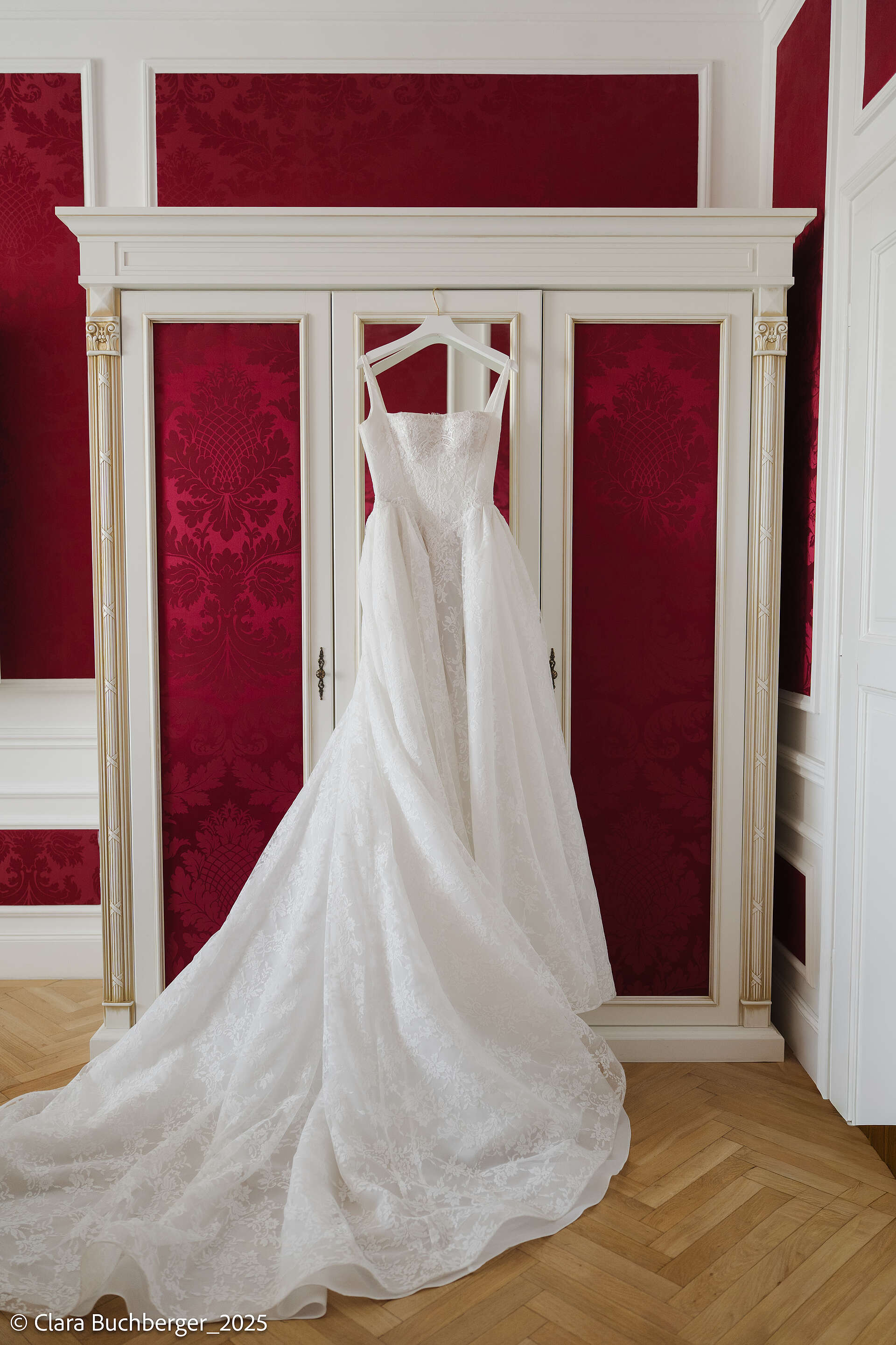 Weißes Brautkleid auf einem Kleiderhaken an der Türe eines mit roten Stammt überzogenen Schranks