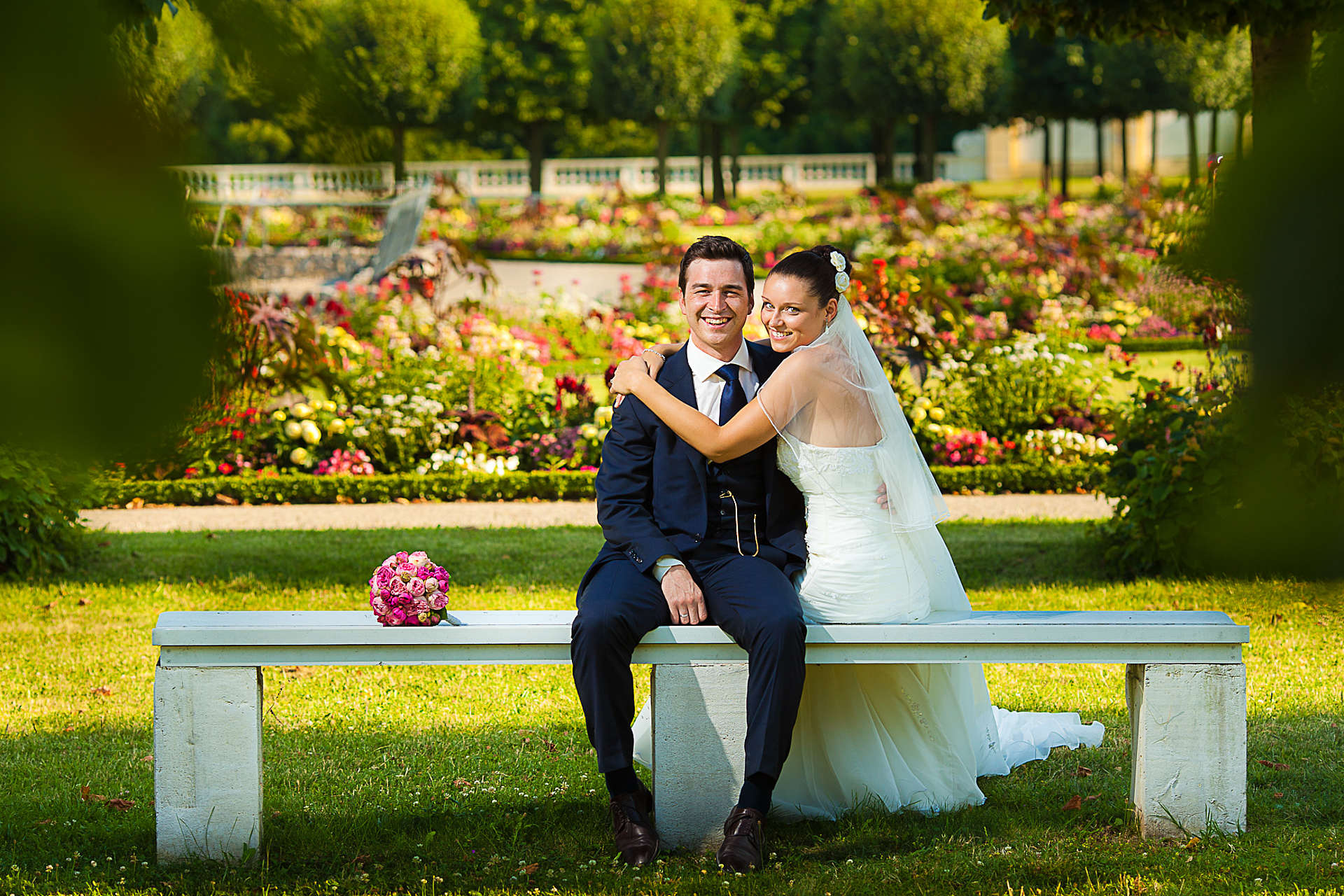 Hochzeitspaar sitzt auf Bank im Barockgarten
